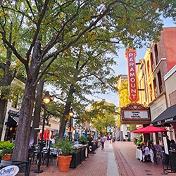 A lively street scene featuring the illuminated Paramount Theater sign, trees, and outdoor dining along a bustling walkway.