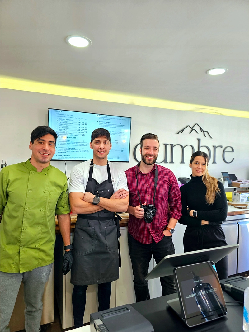 Four people are positioned at a counter, interacting with a laptop that is set on the surface